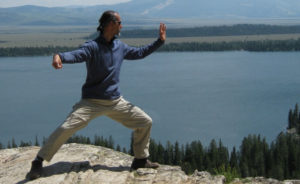 Camilo Sanchez doing tai chi on a mountain overlooking a lake.